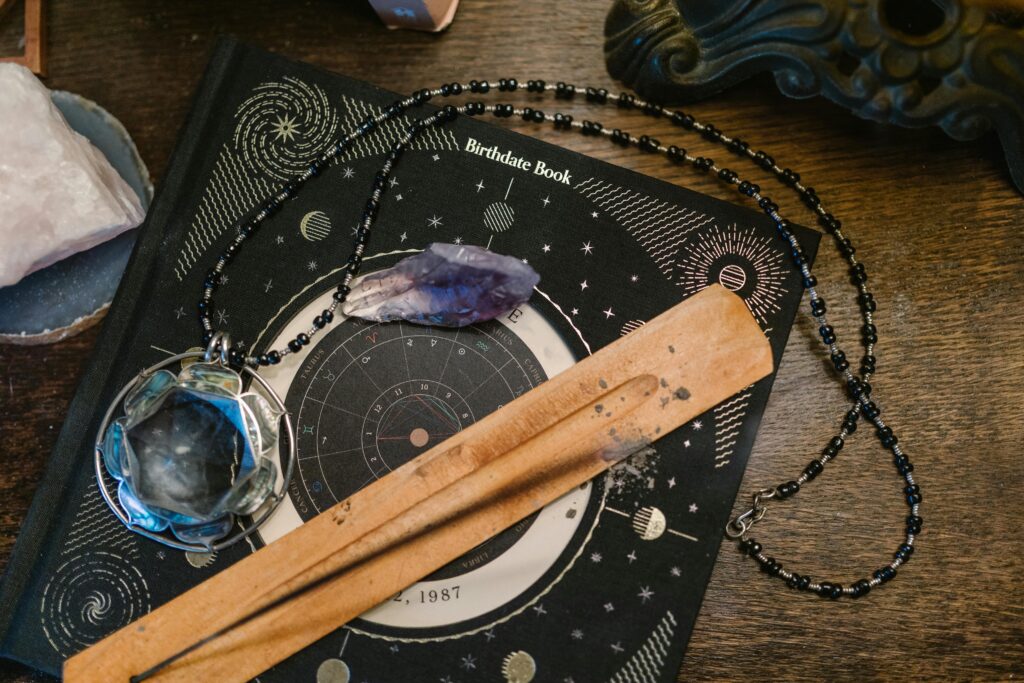 pexels-photo-6806400-6806400-1 Astrology-themed flat lay featuring a birthdate book, crystals, and necklace on a wooden surface.