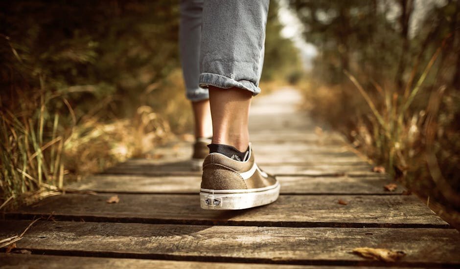 Person wearing sneakers walking on a wooden path in a sunlit park.