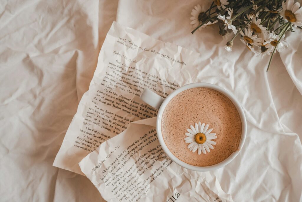 A cup of coffee with a daisy on a bed of book pages and flowers, creating a cozy, artistic scene.