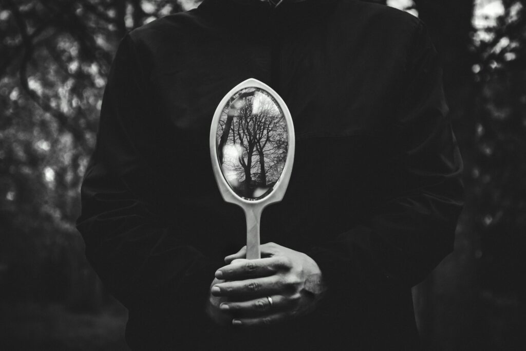 A person holding a mirror reflecting bare trees in a black and white setting.