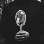 A person holding a mirror reflecting bare trees in a black and white setting.