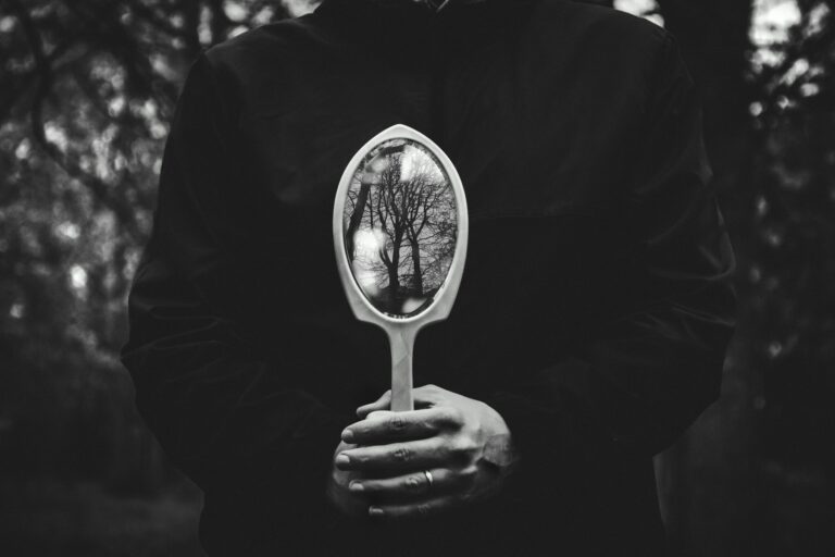 A person holding a mirror reflecting bare trees in a black and white setting.
